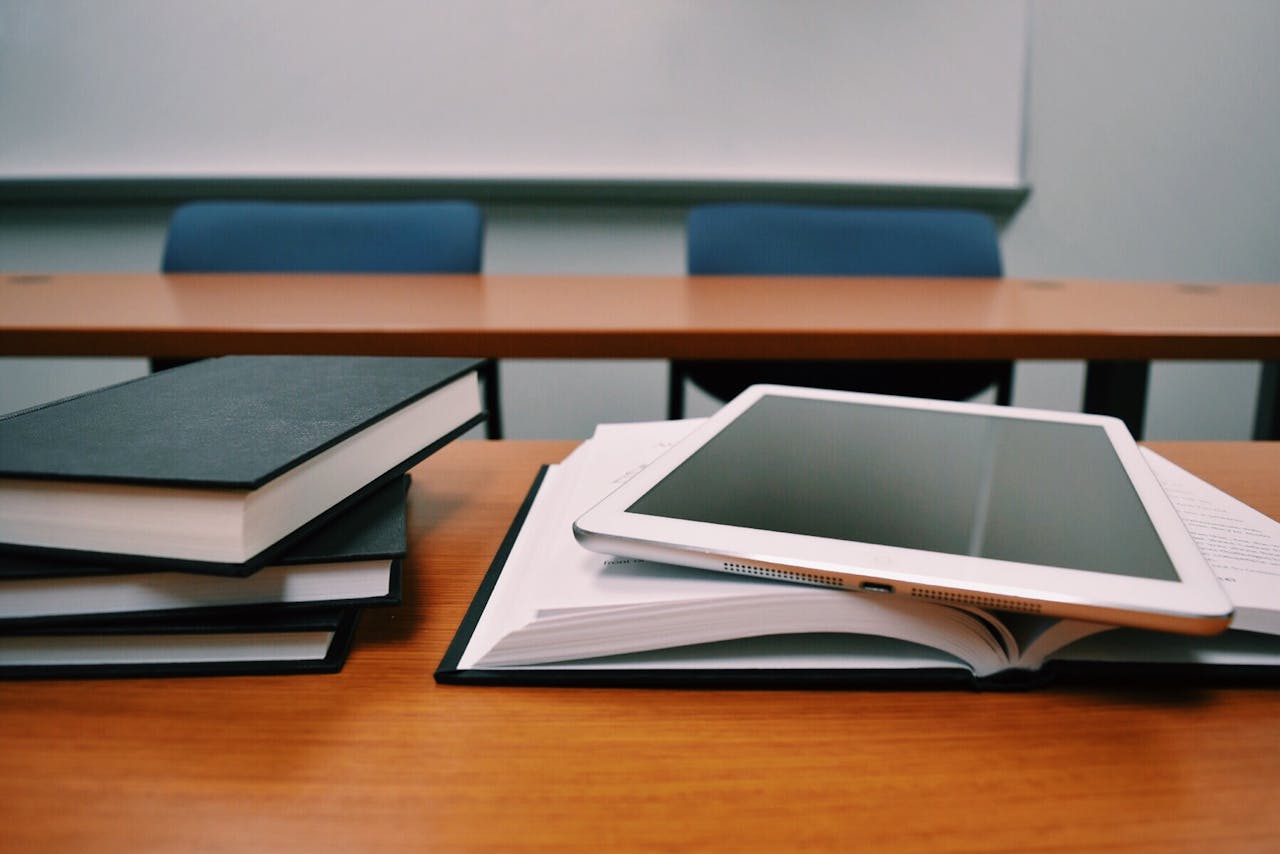 our-history-img Books and a tablet on a desk in a classroom, depicting modern education.